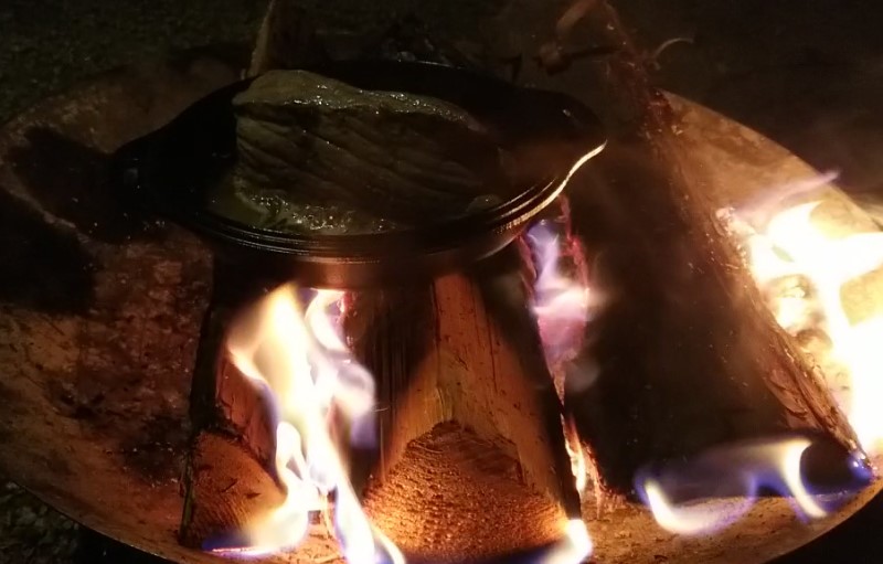 焚き火の上でスキレット調理。豪快に焼かれる肉。